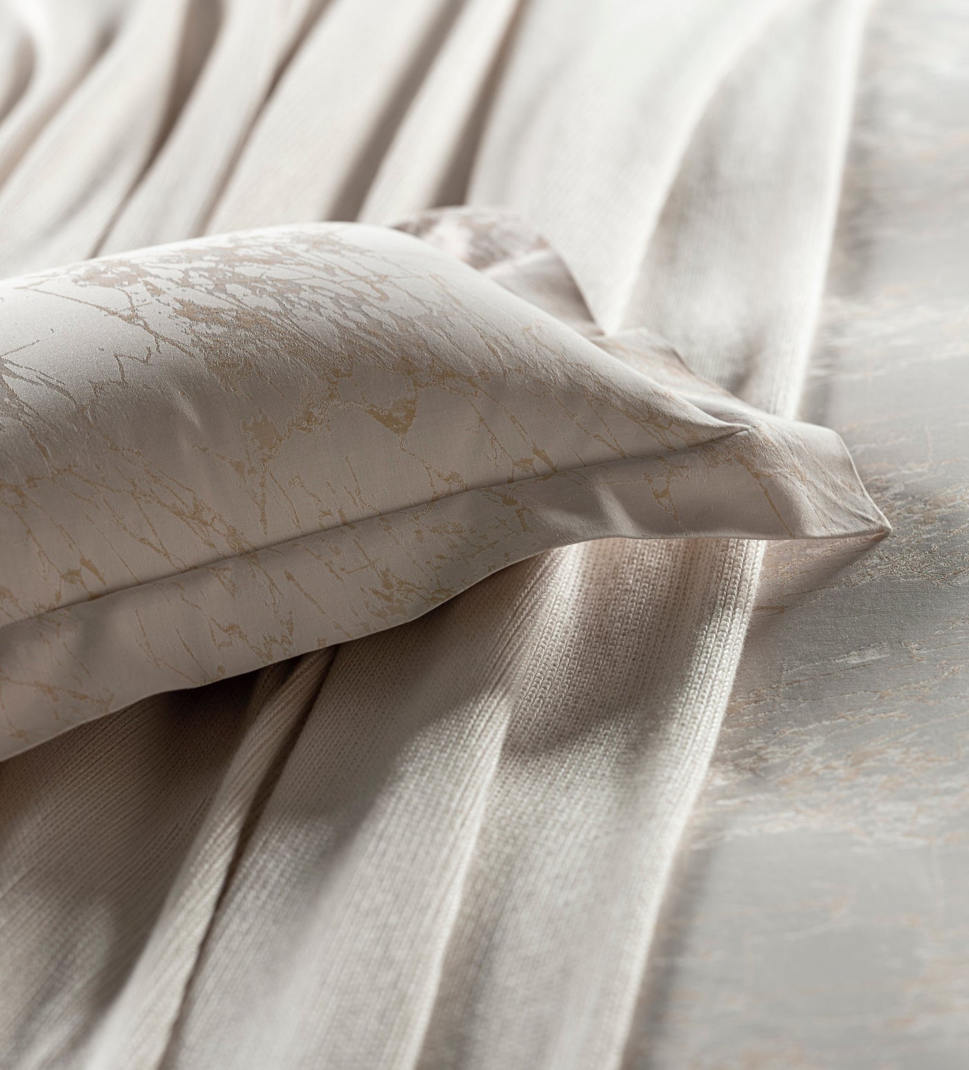 Close-up of ivory Celso de Lemos Parus pillowcase with gold marbled print against draped champagne bedding.