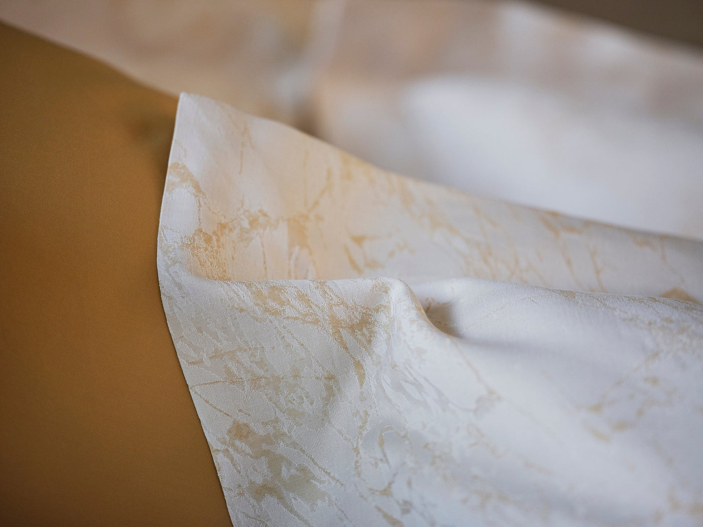 Close-up of Celso de Lemos Parus pillowcase hem, ivory jacquard with champagne botanical pattern.