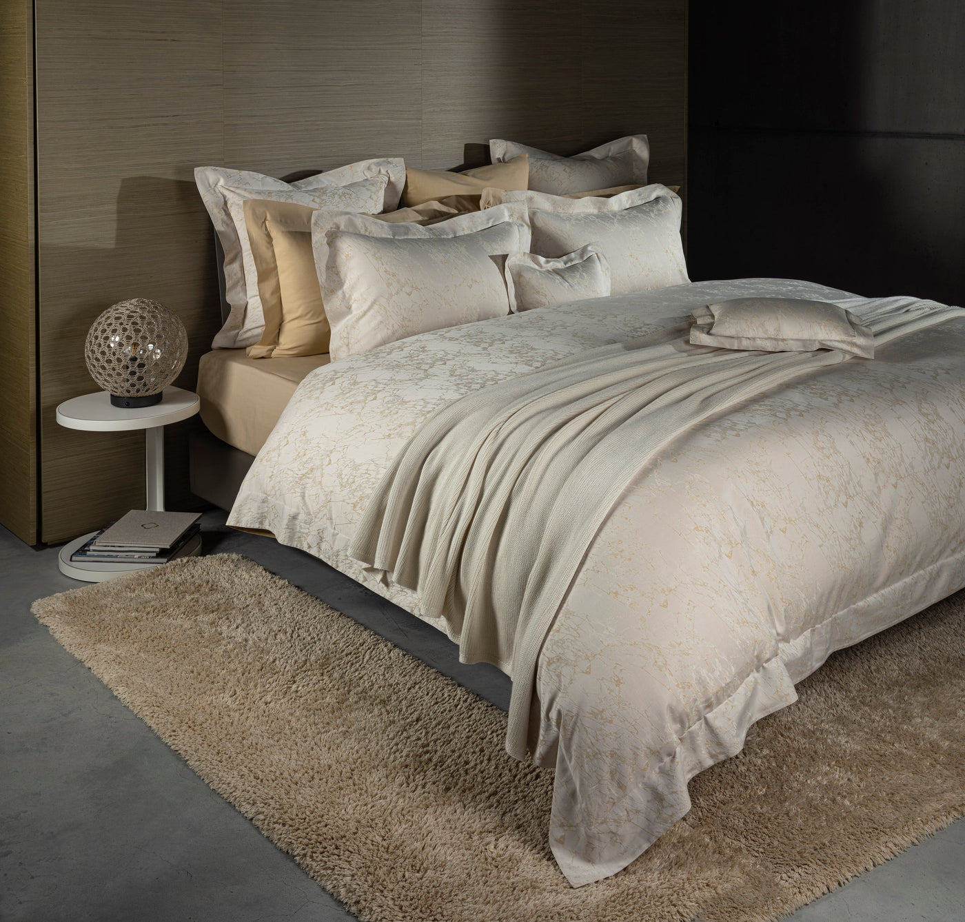 Styled bed showing Parus pillowcase layered with champagne and ivory bedding in a dark bedroom.