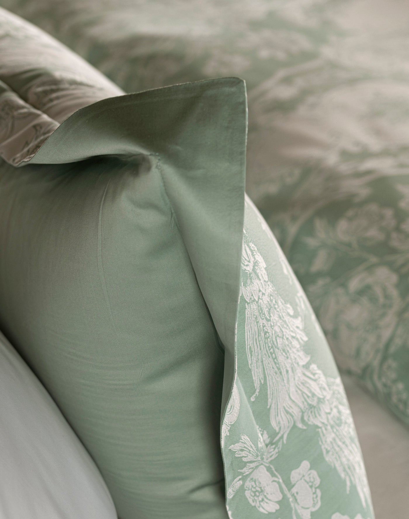 Close-up of sage green pillowcase corner revealing floral jacquard reverse pattern.