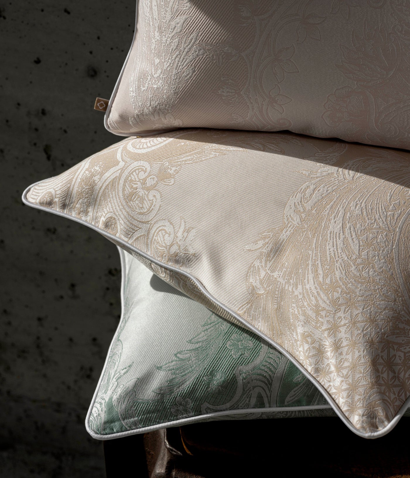 Close-up of stacked Celso de Lemos Pompadour pillowcases in ivory and sage with ornate paisley jacquard.