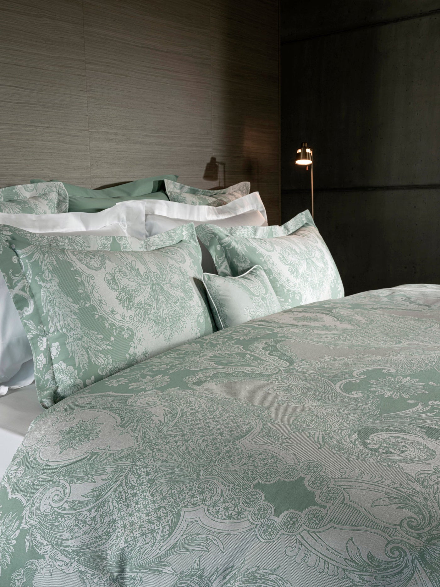 Sage green damask pillowcase detail, ornate baroque jacquard pattern on layered bedding.