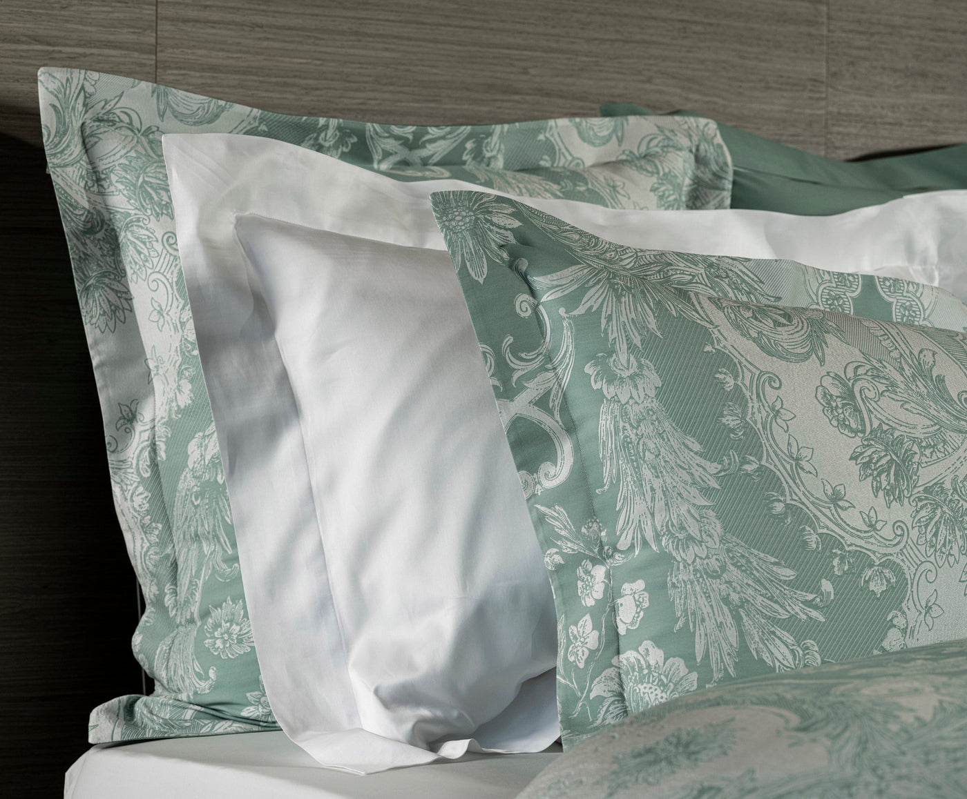Close-up of Celso de Lemos Pompadour pillowcase in sage, baroque damask print layered with white shams.