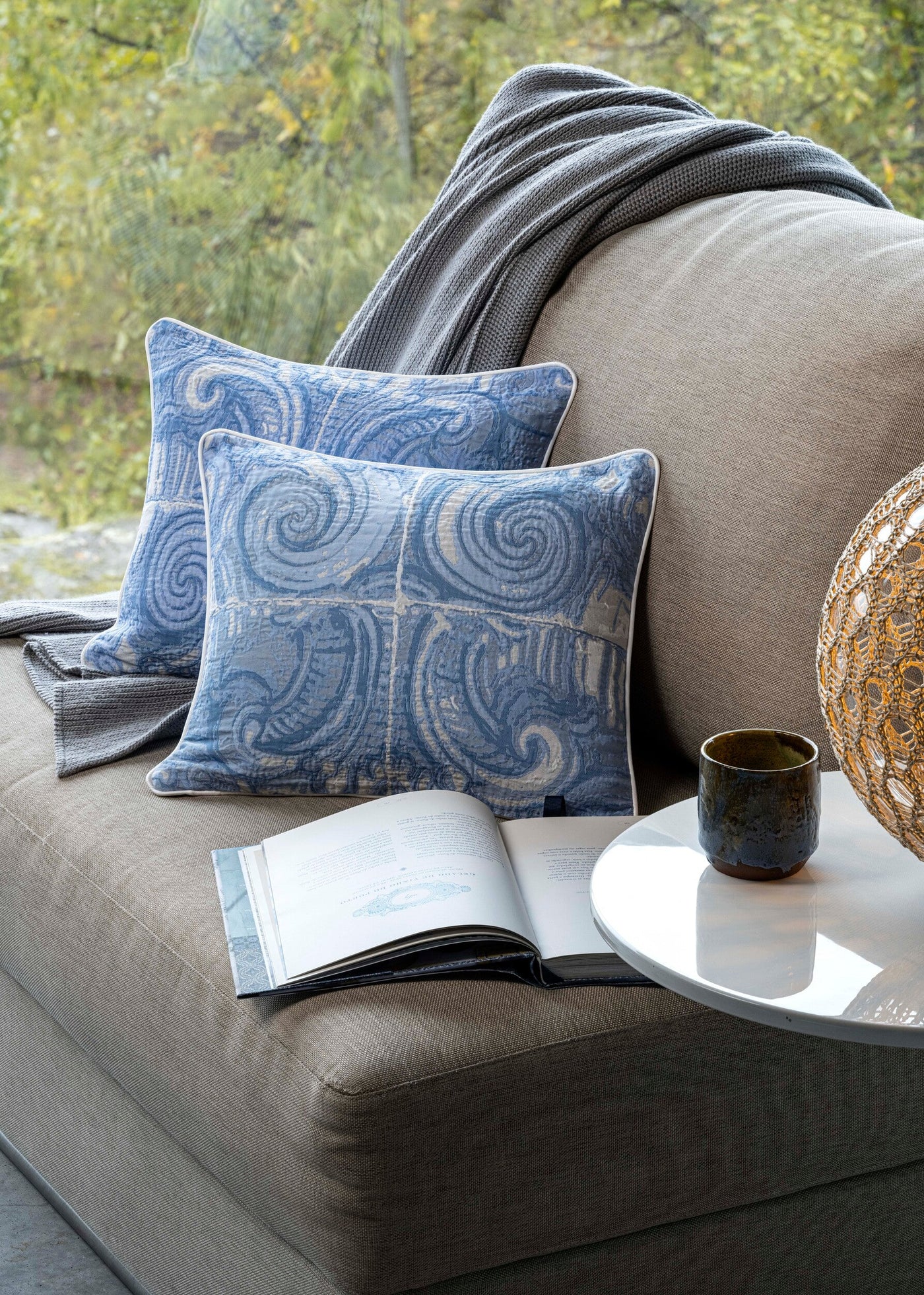 Celso de Lemos Porto pillow covers in blue swirl pattern styled on a grey sofa.
