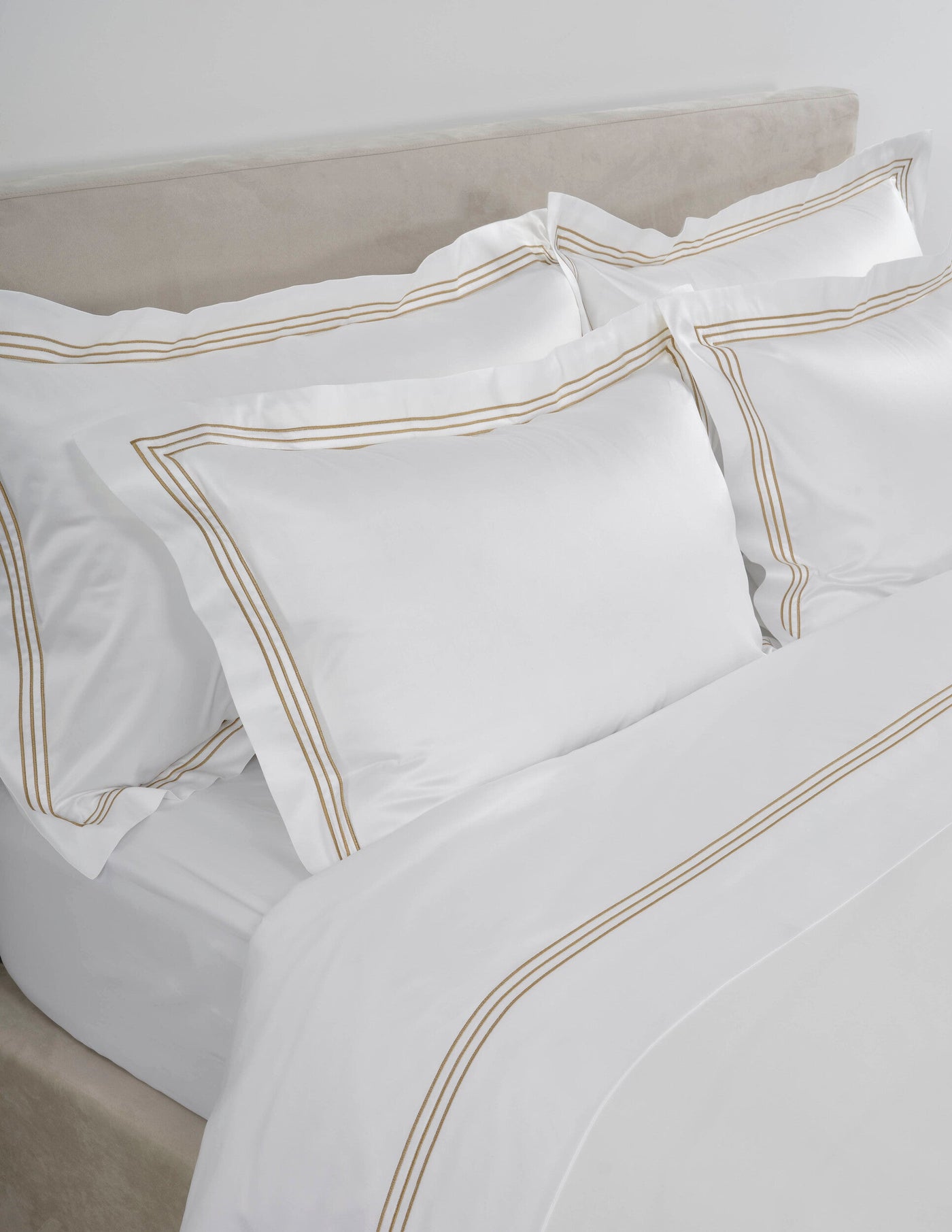 Angled view of white duvet cover with triple gold embroidered border detail.