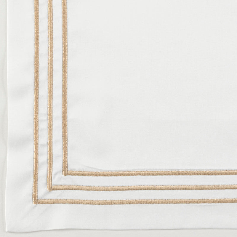 Close-up of white duvet cover corner with double gold embroidered border trim.