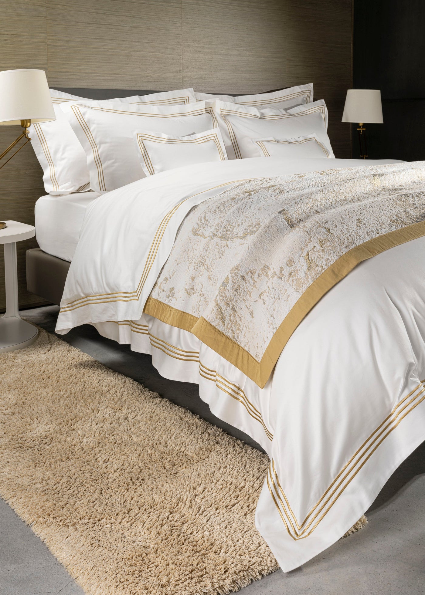 Angled view of white flat sheet with gold stripe border, styled on a made bed.