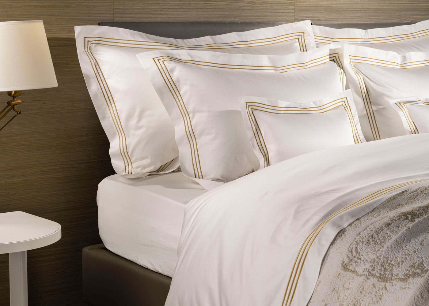 Close-up of white flat sheet with triple gold satin stitch border, styled on a made bed.