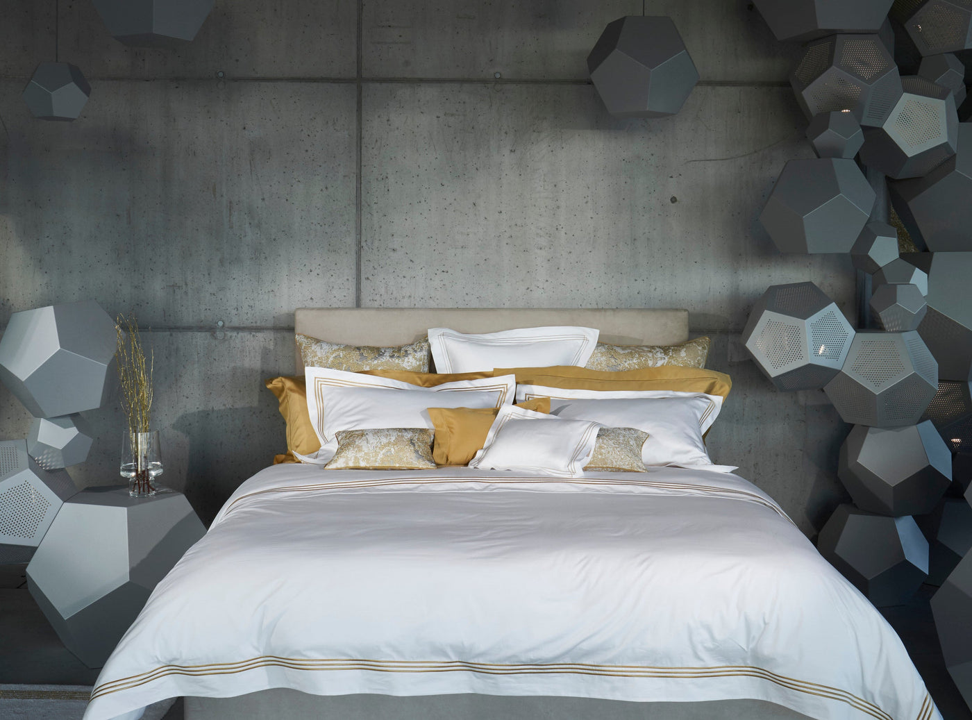 Bed styled with white and gold Ram flat sheet against a concrete wall with geometric decor.