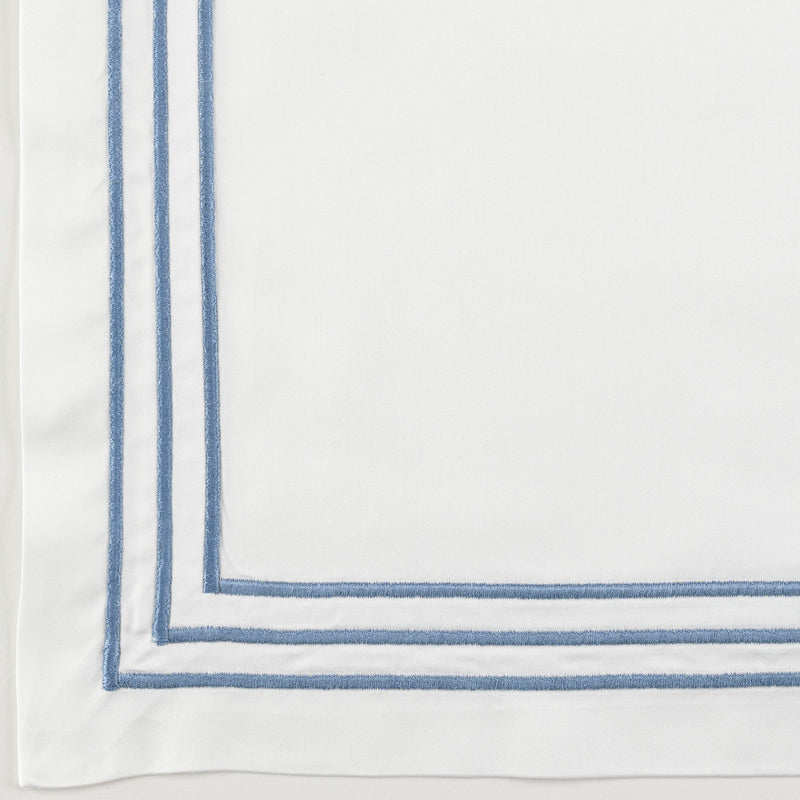 Close-up of white flat sheet corner with double blue embroidered border trim.