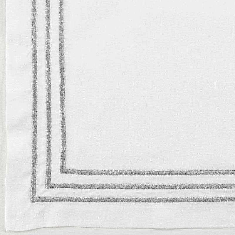 Corner detail of white flat sheet with double silver embroidered border trim.