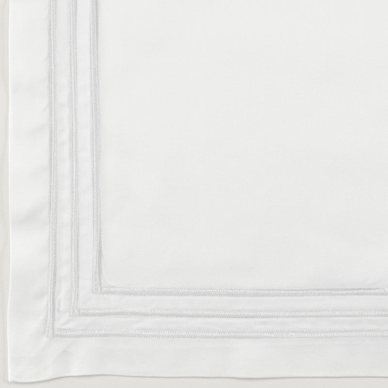 Close-up of Ram flat sheet corner with double silver embroidered border on white cotton.
