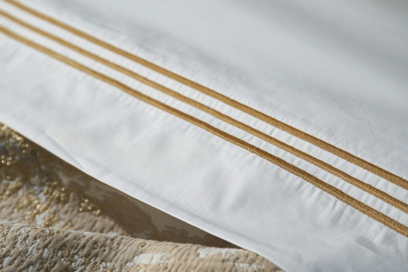 Close-up of white pillowcase hem with three parallel gold satin stripes.