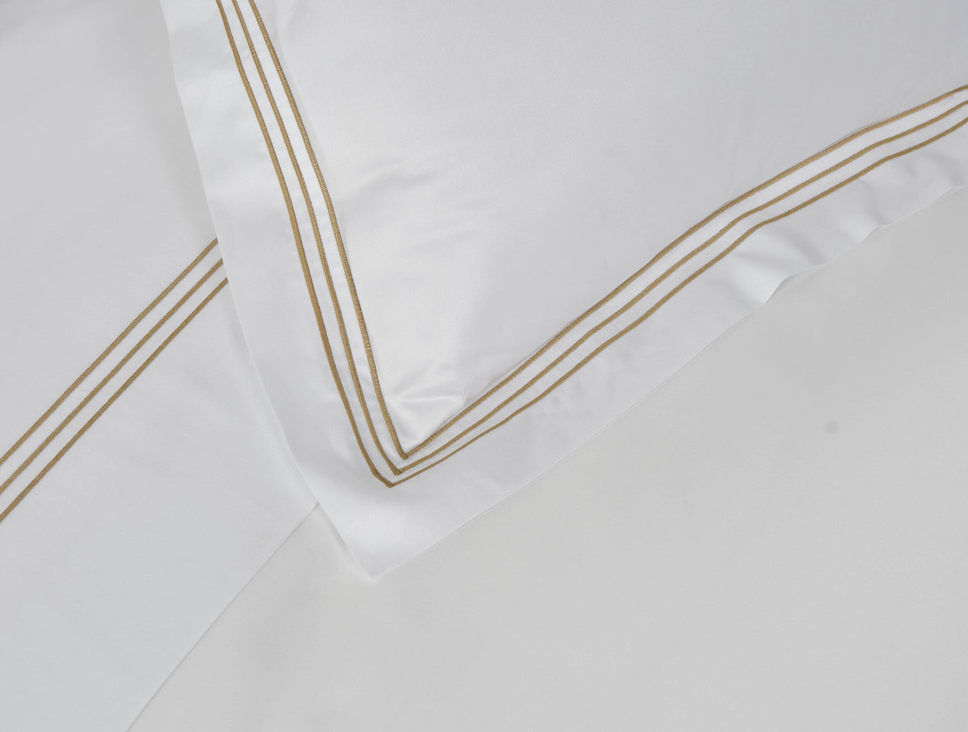Close-up of white pillowcase corner with triple gold embroidered stripe border detail.
