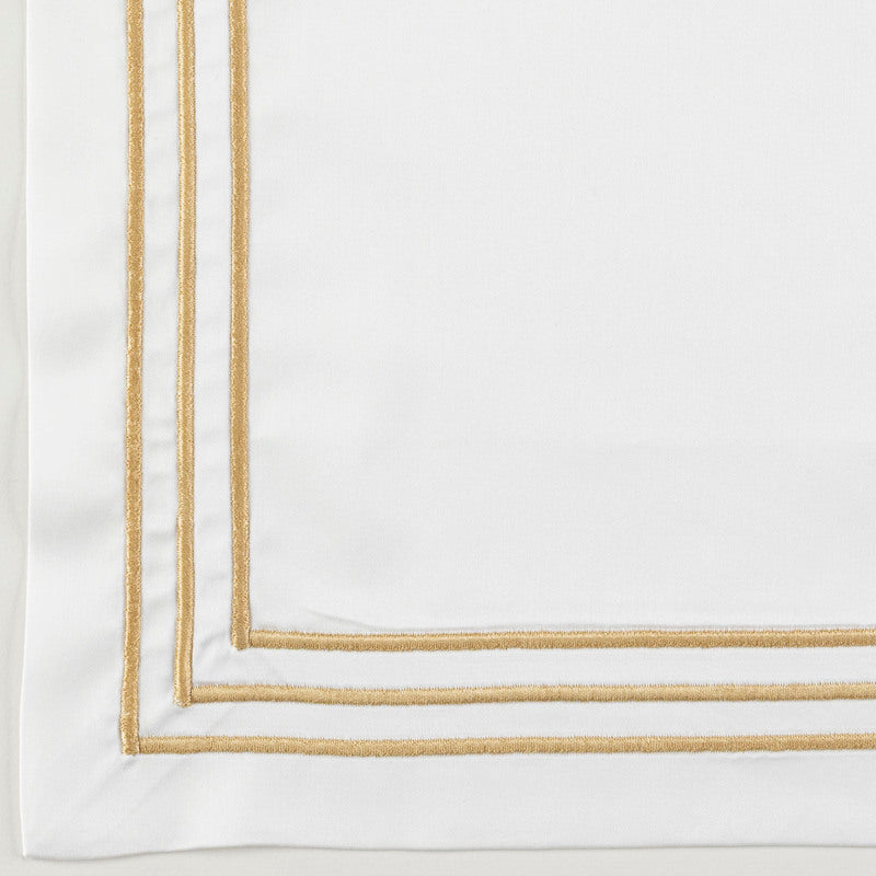 Corner detail of white pillowcase with double gold embroidered border trim.