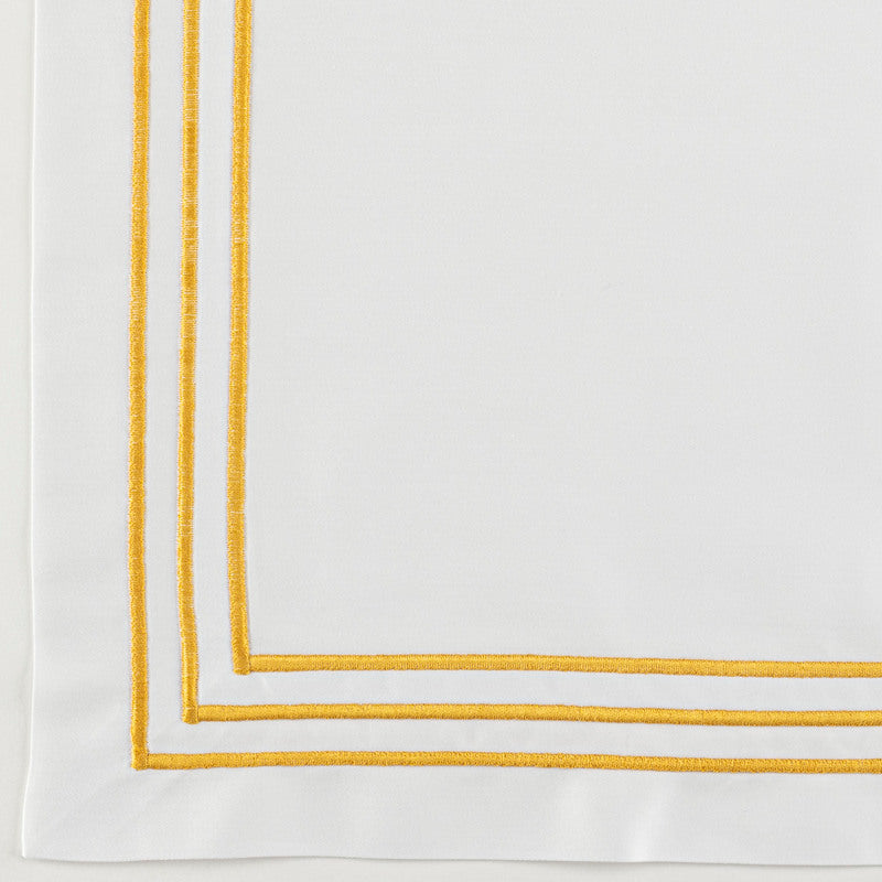 Corner detail of white pillowcase with double golden yellow embroidered border trim.