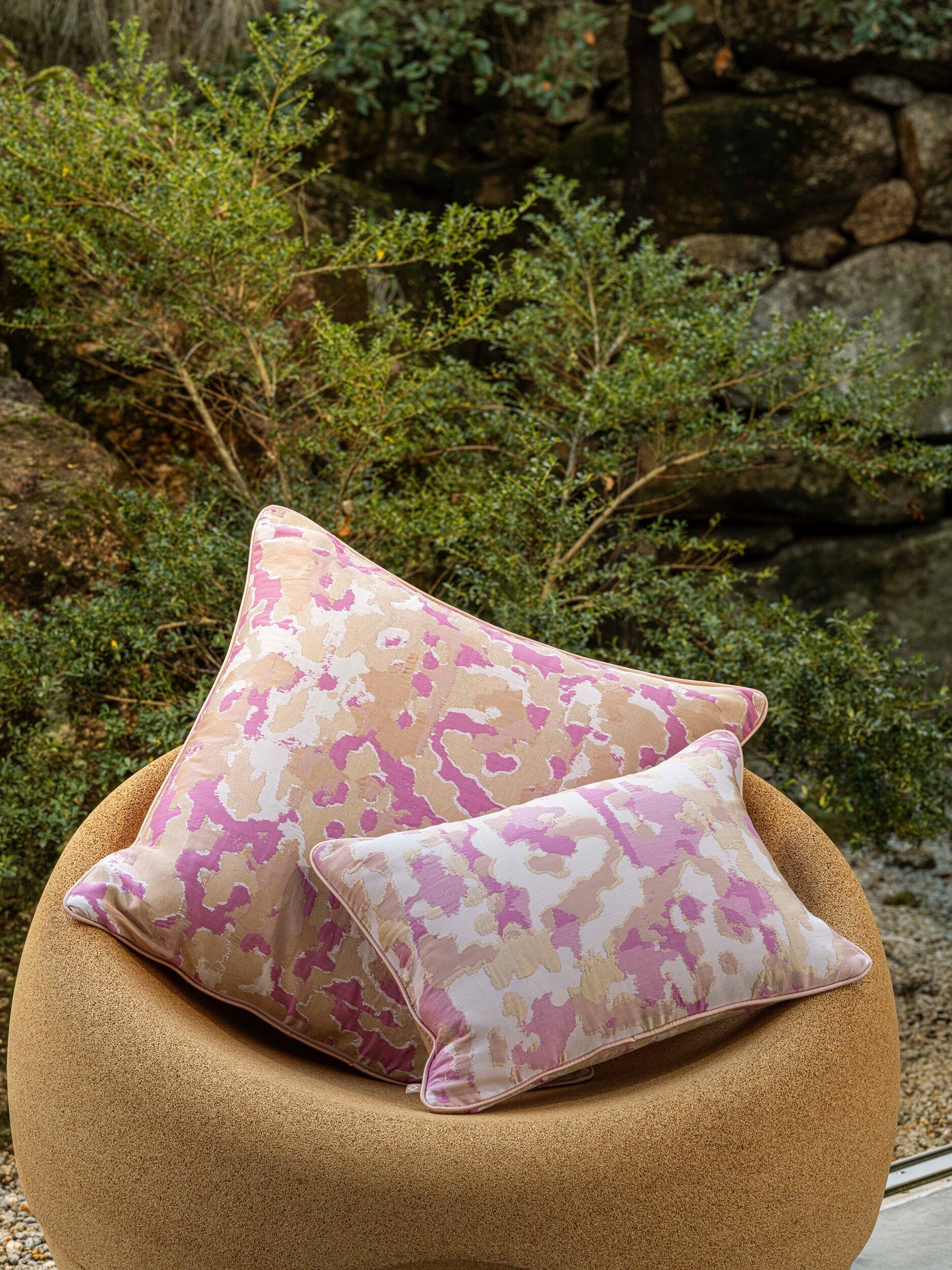 Two Celso de Lemos Rosa pillow covers in pink floral print, stacked on a round camel chair outdoors.