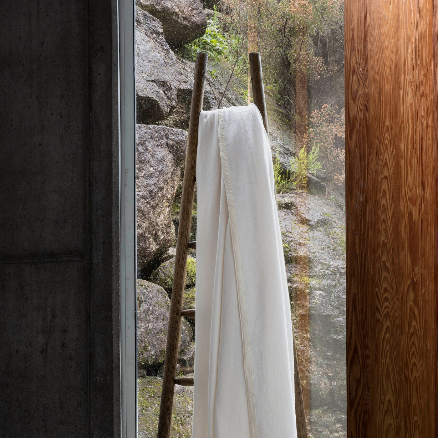 White garment hanging on a wooden ladder with a natural rock and forest background