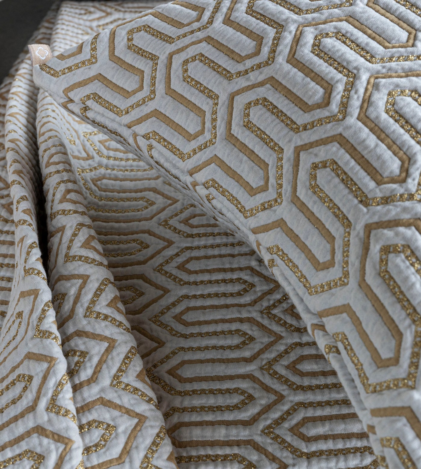 Close-up of Vendome pillow sham showing gold geometric hexagon embroidery on ivory fabric.