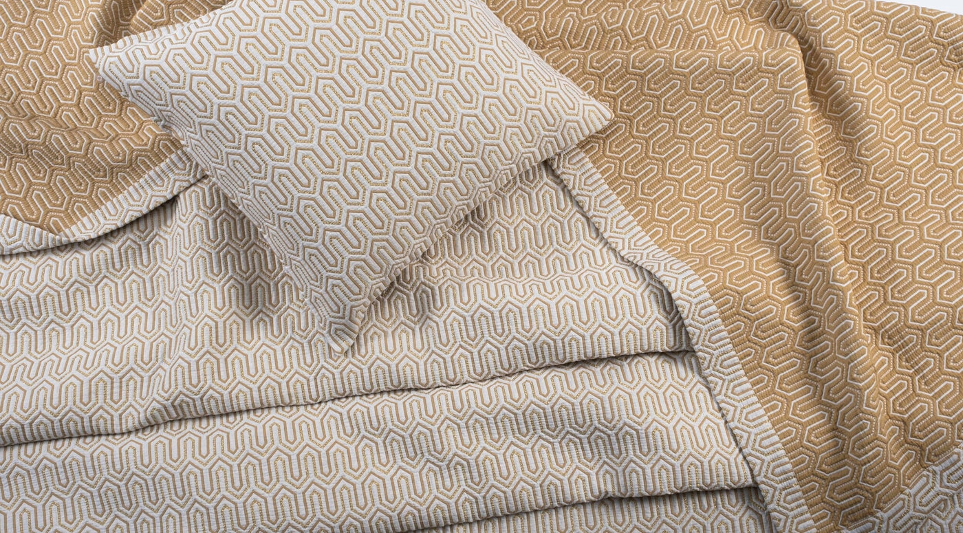 Close-up of Vendome pillow cover and draped bedding in gold geometric honeycomb pattern.