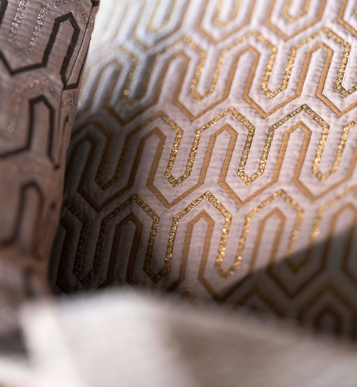 Close-up of Vendome pillow covers with gold geometric hexagonal embroidery on ivory fabric.