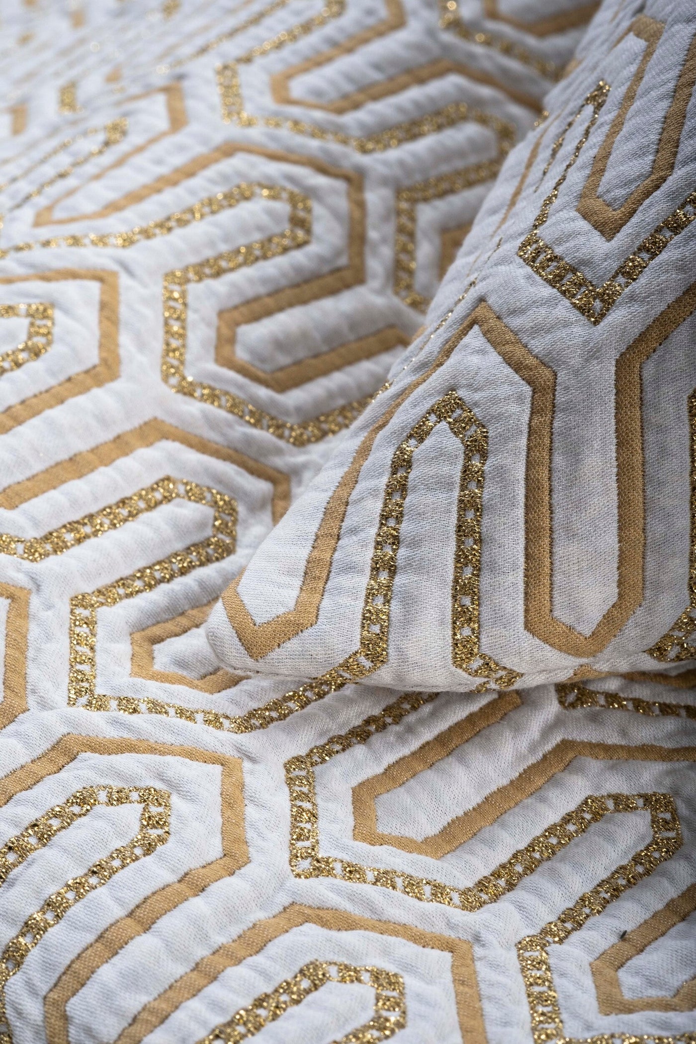 Close-up of ivory fabric with gold geometric hexagonal embroidery and metallic thread detail.