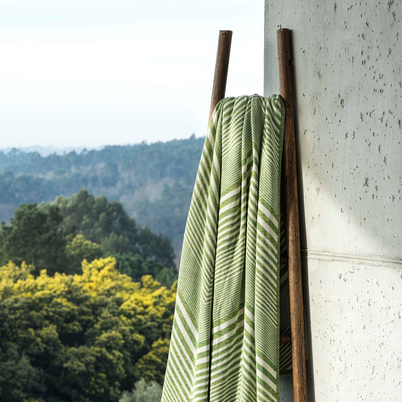 Green striped towel on a wooden ladder against a stone wall with a scenic background