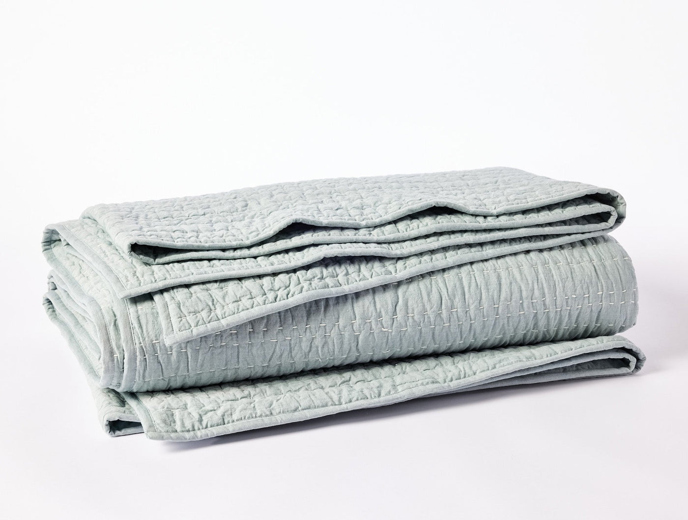 Close-up of folded Coyuchi Channel Handstitched quilt in pale sage with textured stitching.