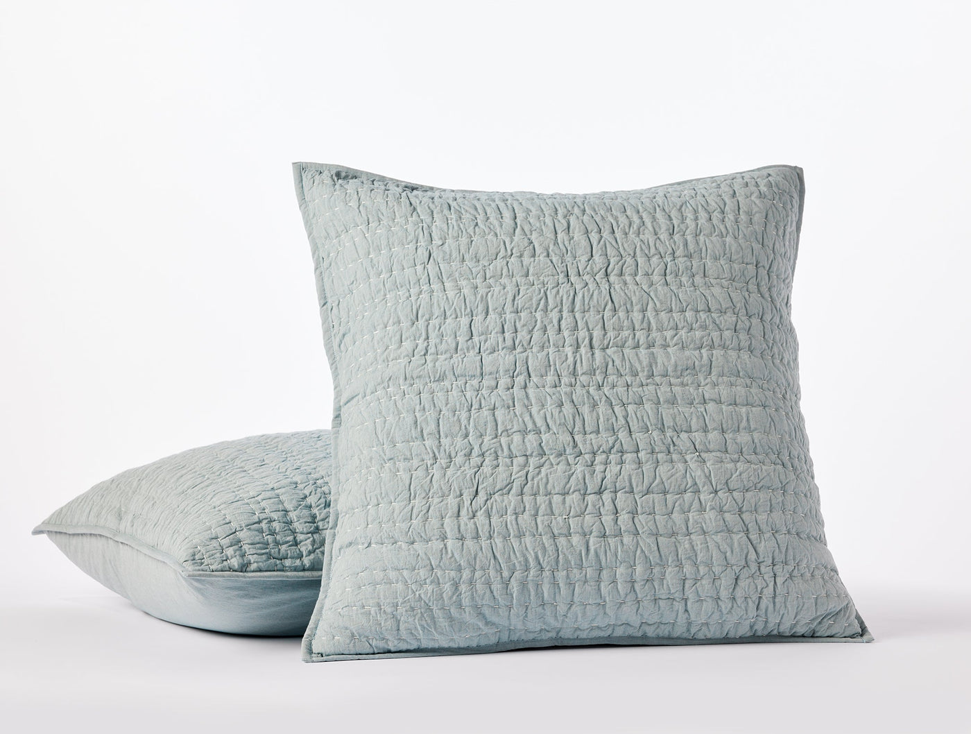 Close-up of two stacked Coyuchi Channel Handstitched shams in mist blue with quilted texture.