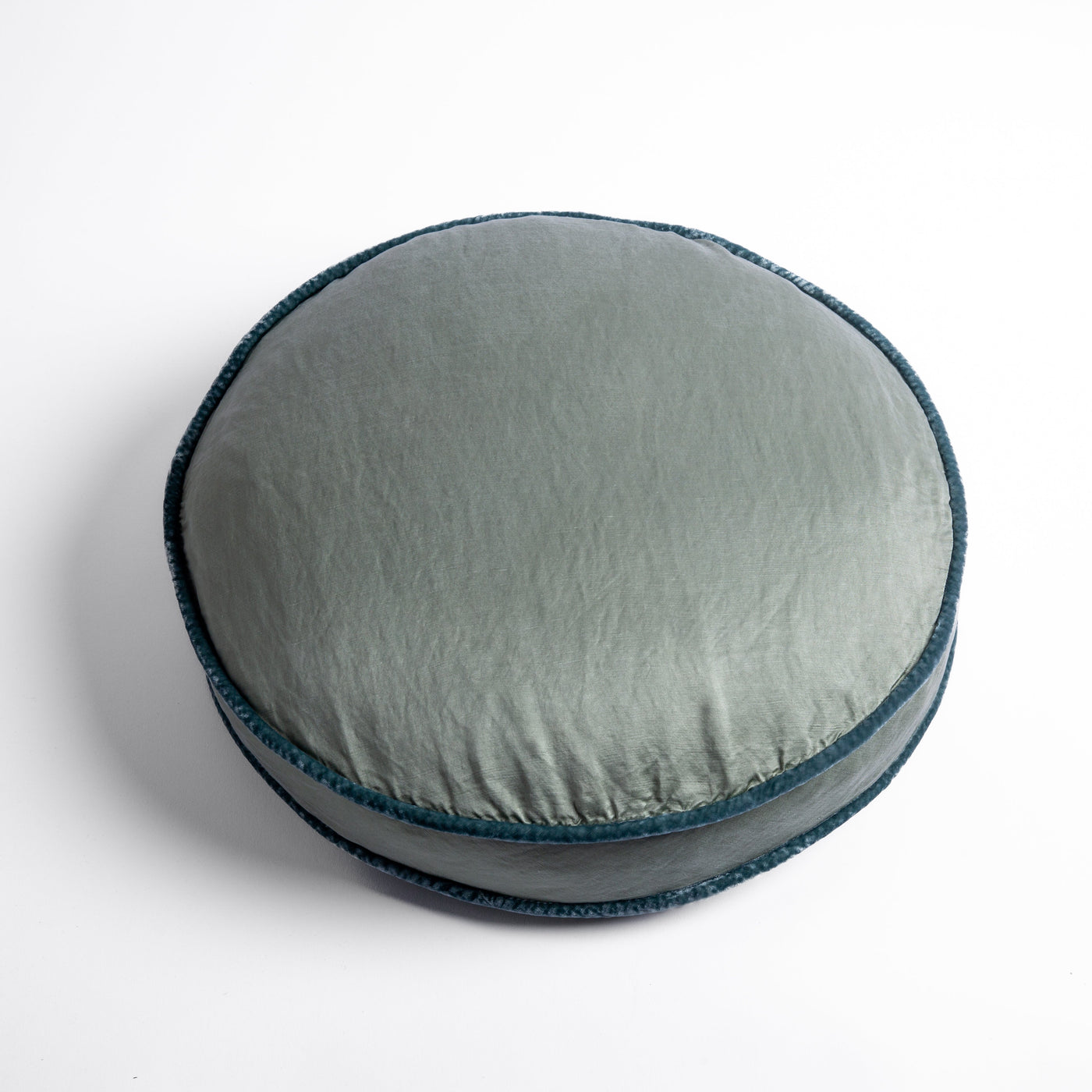 Round Paloma throw pillow in Eucalyptus with teal braided trim, top-down angle.