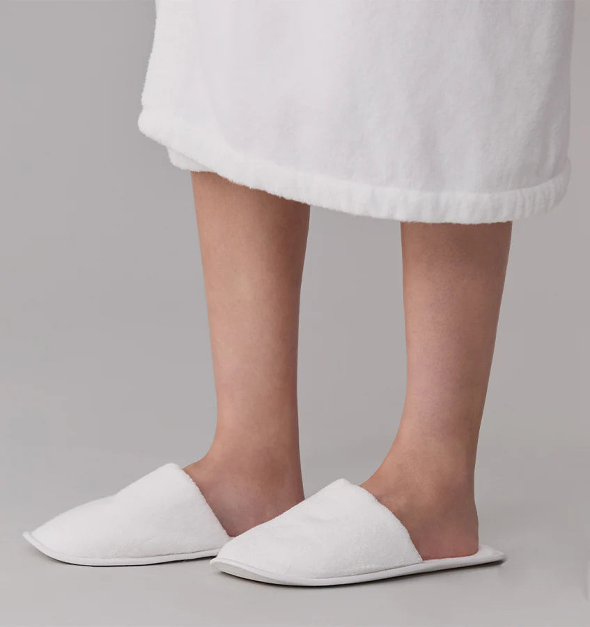White slippers worn with a white bathrobe on a neutral background