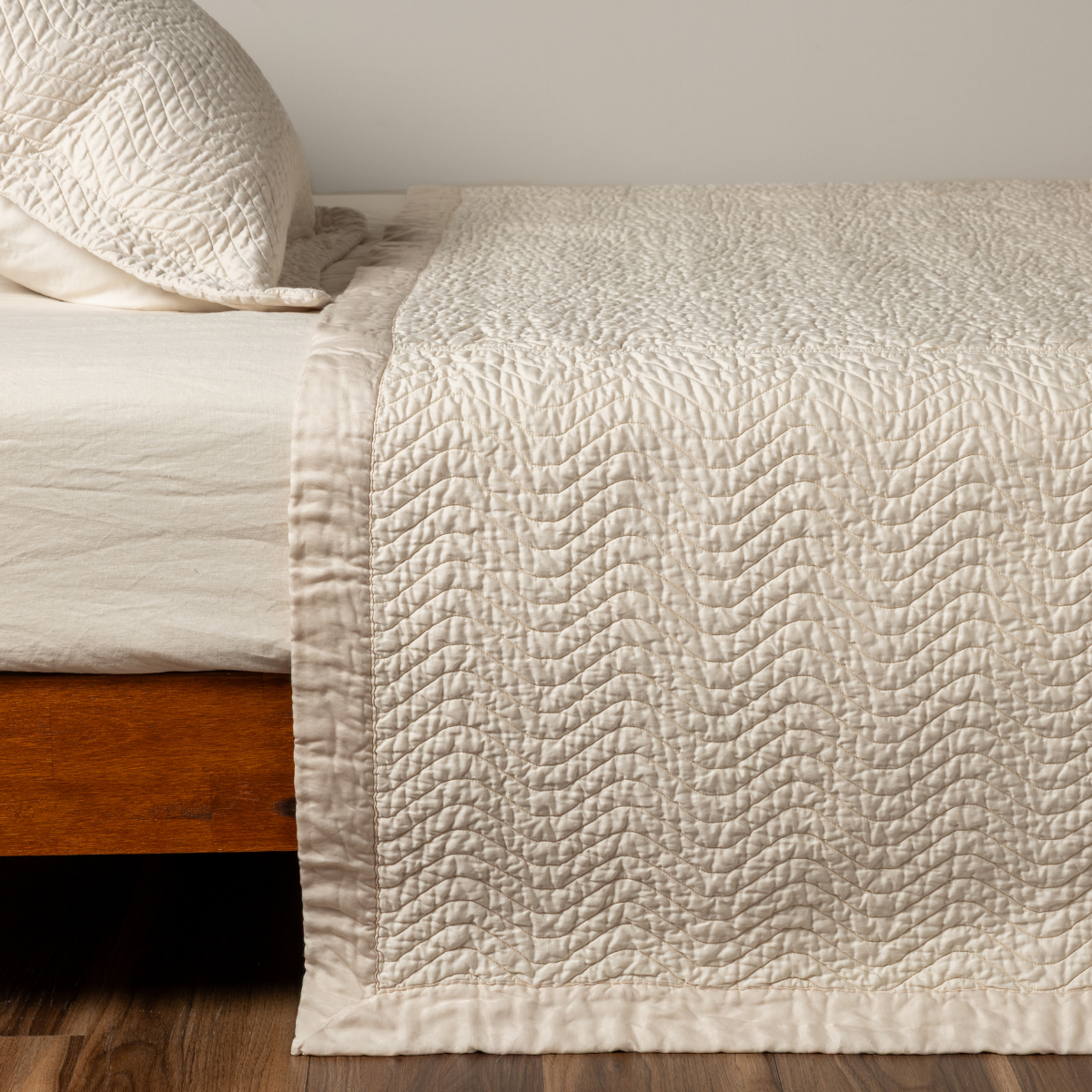 Bella Notte Cirillo coverlet in Natural, showing quilted wave stitching detail draped over bed corner.