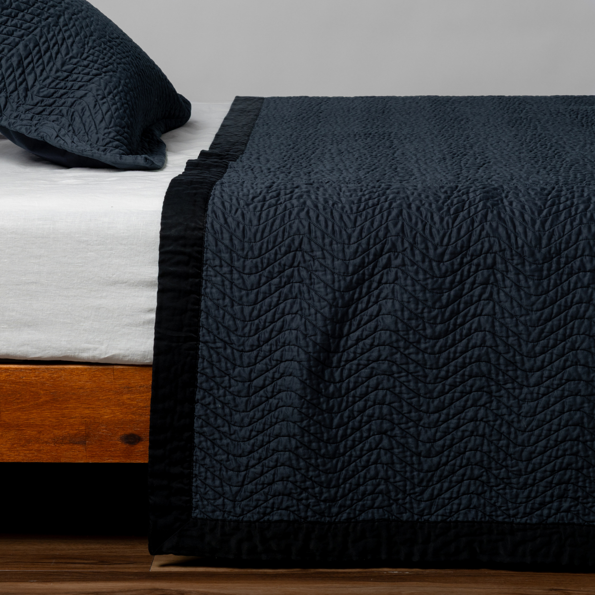 Slate Cirillo coverlet draped over bed corner, showing quilted leaf pattern and ruffled edge detail.