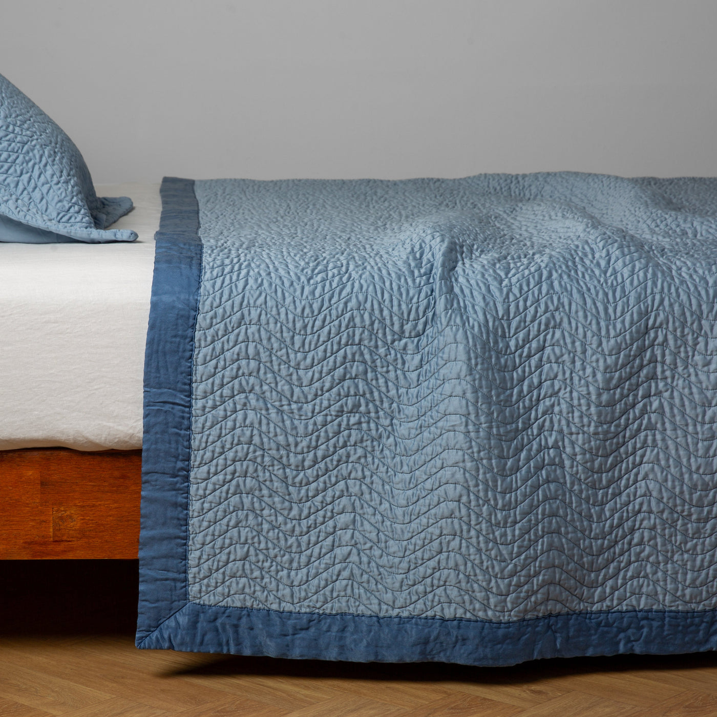 Bella Notte Cirillo coverlet in Tahoe Blue draped over bed, quilted leaf pattern with contrast border.