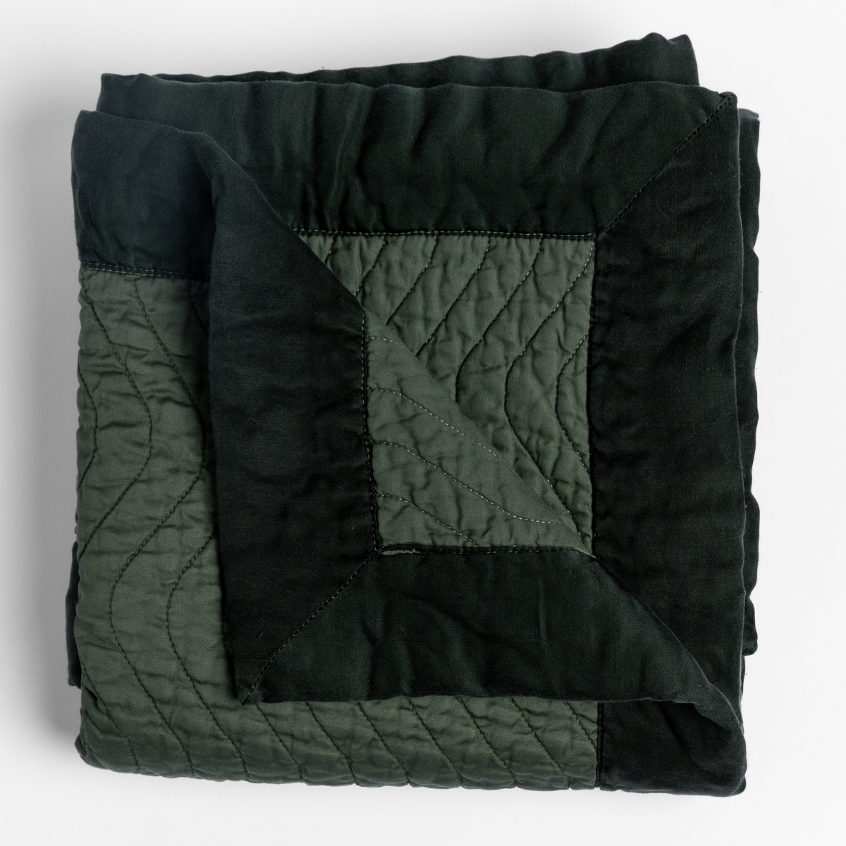 Folded Juniper Cirillo throw, showing quilted texture and two-tone dark green colorblocked panels.