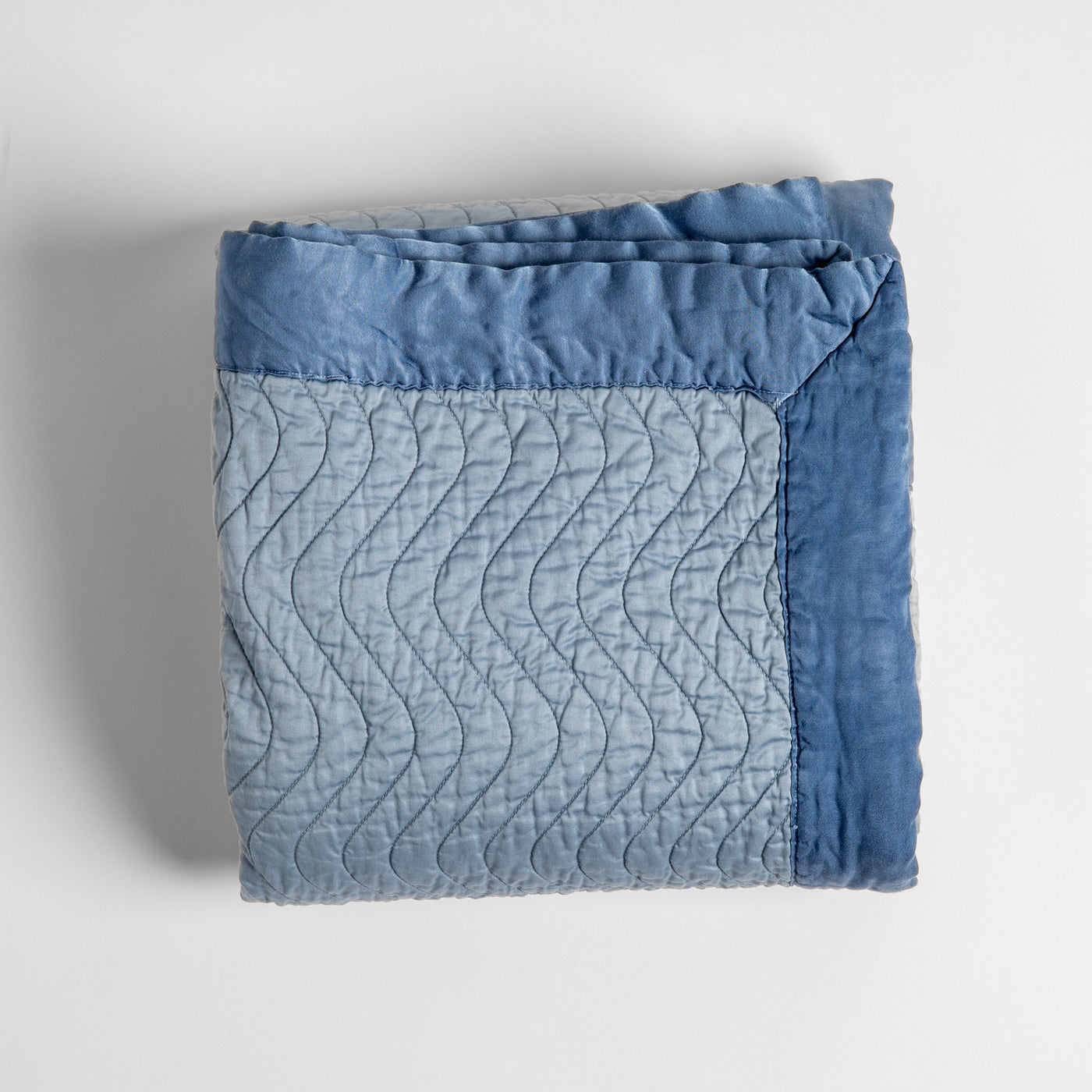 Folded Tahoe Blue quilted velvet throw, wave-stitched face with contrasting border detail.
