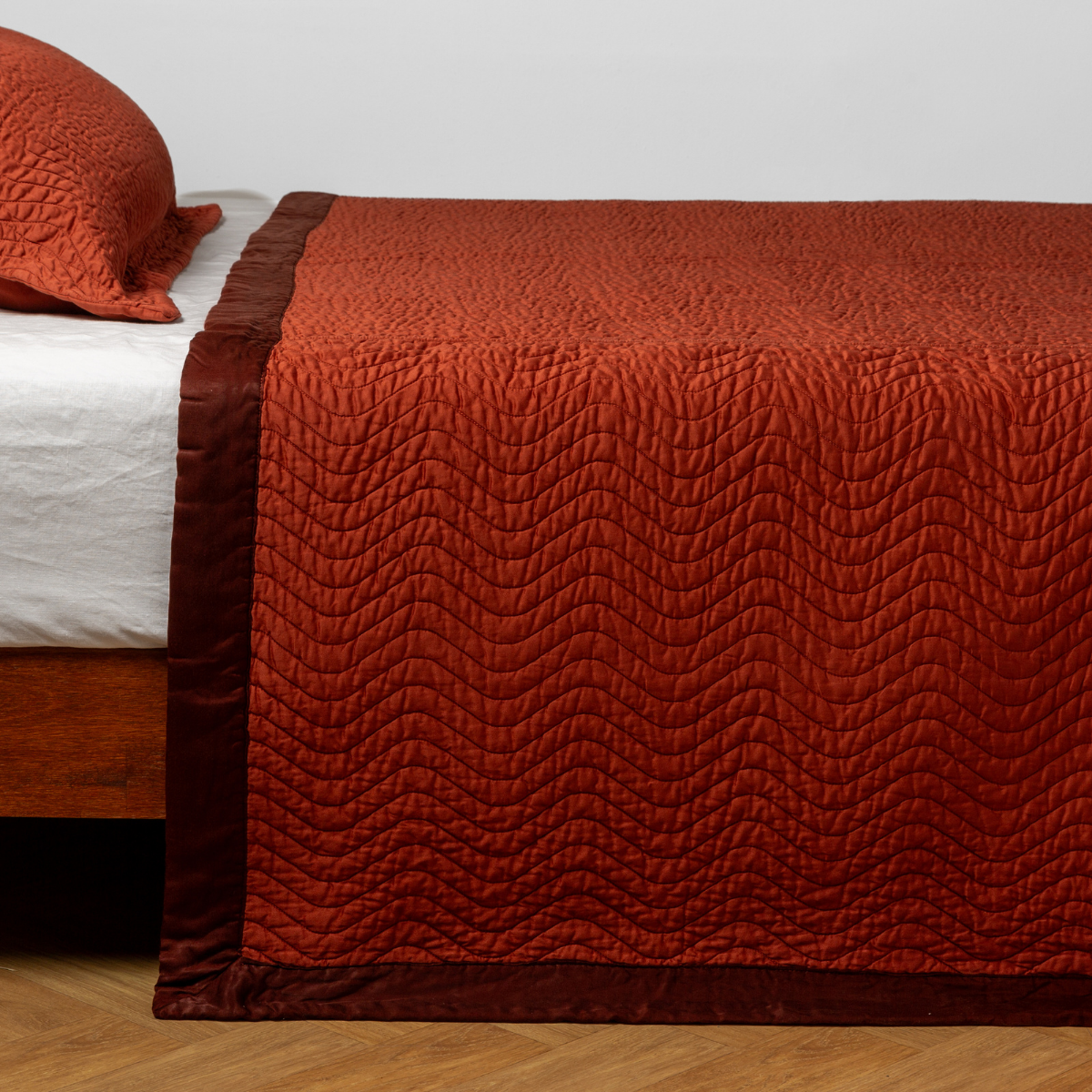 Autumn coverlet draped over bed, wave quilting pattern with deep burgundy border trim.