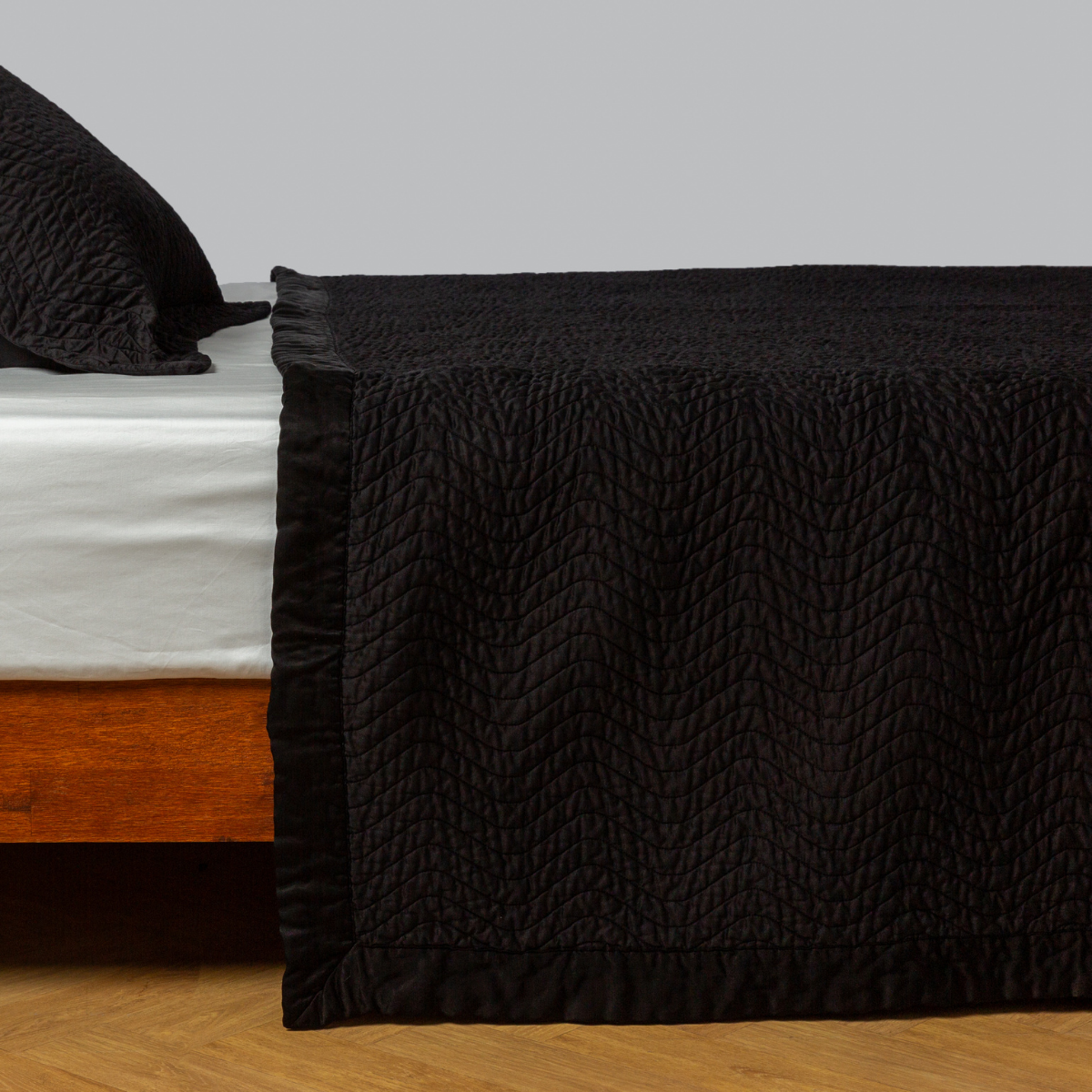 Cirillo coverlet in Corvino draped over bed, showing quilted texture and satin trim detail.
