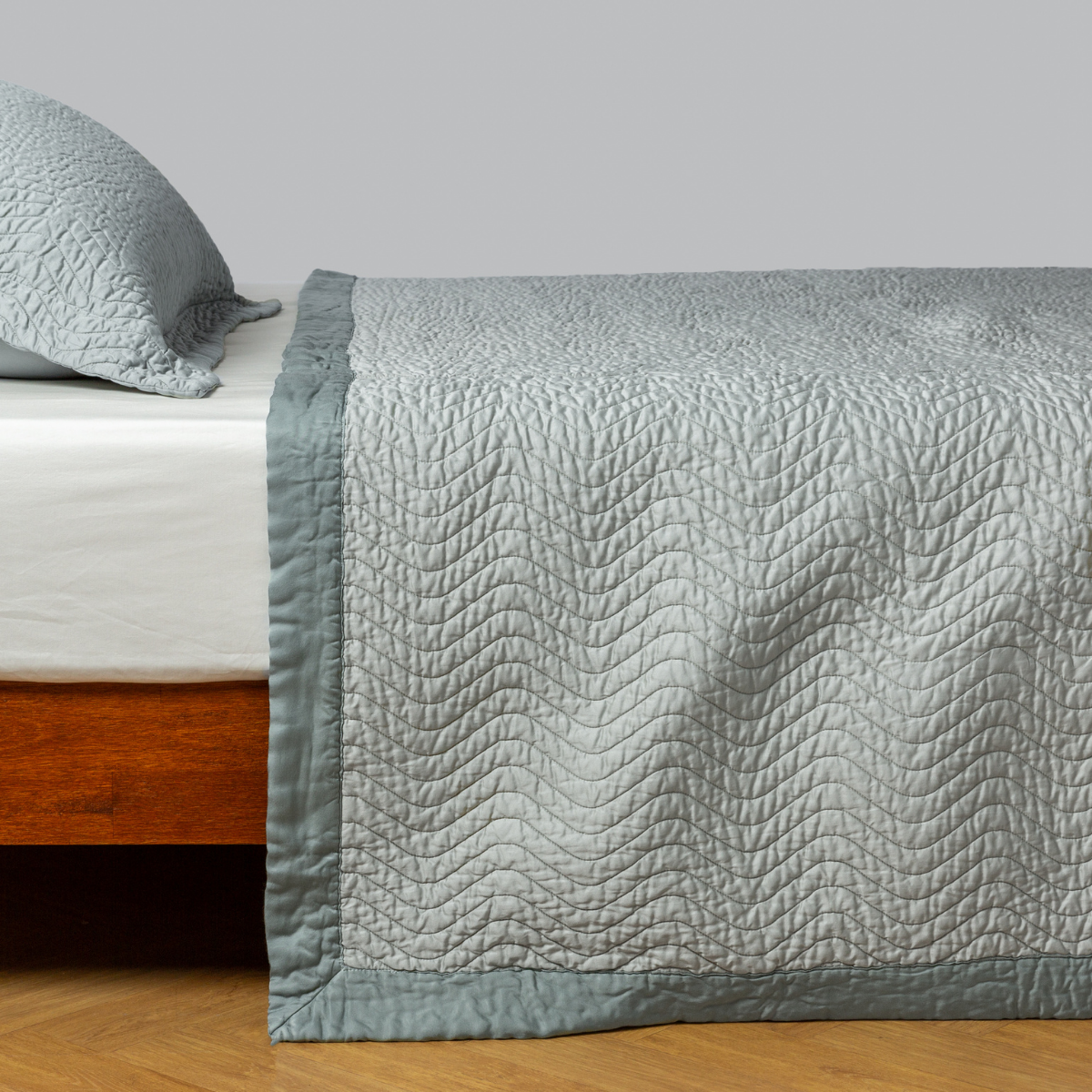 Bella Notte Cirillo coverlet in Eucalyptus draped over bed, showing quilted wave texture and border detail.