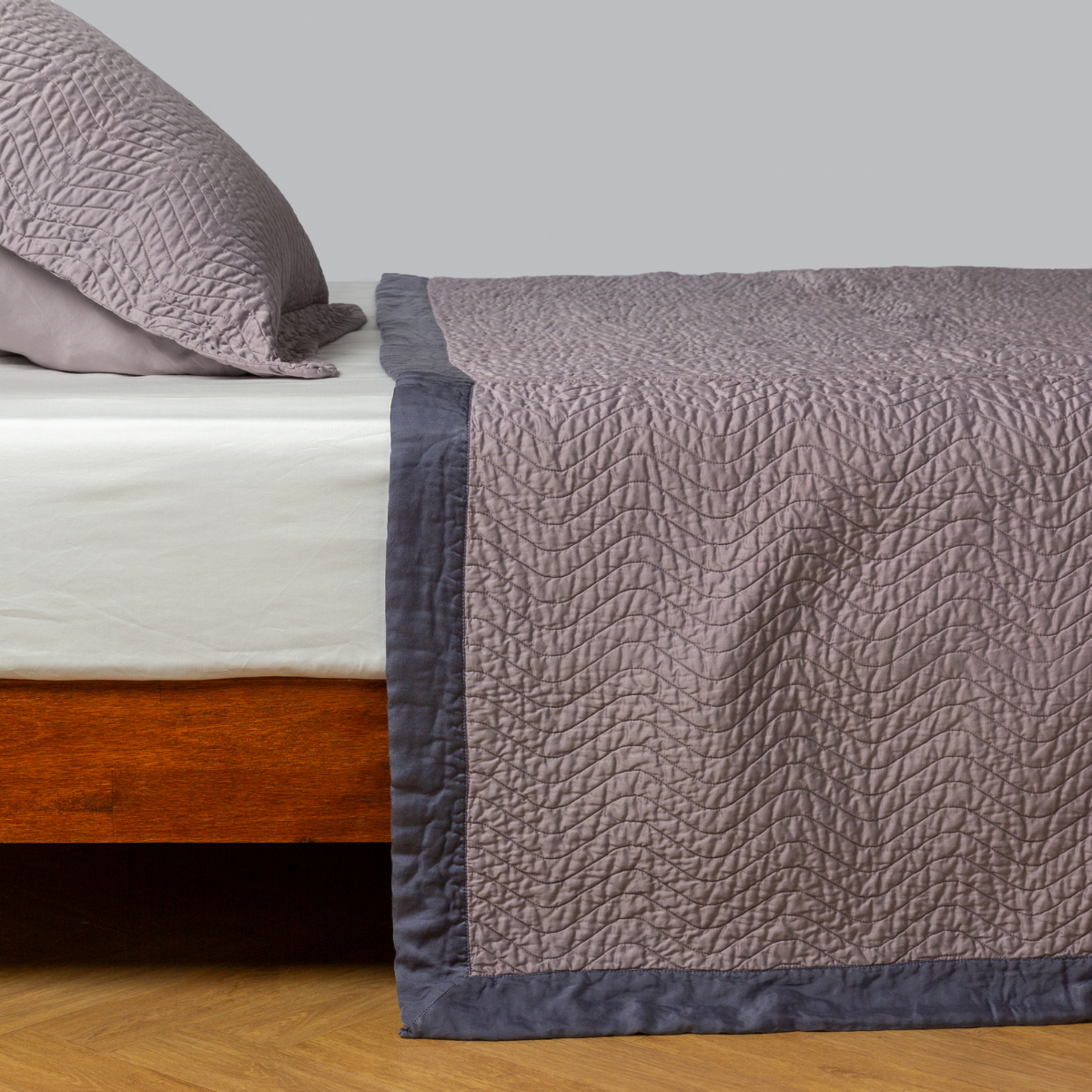 Bella Notte Cirillo coverlet in French Lavender draped over bed foot, showing contrast border detail.