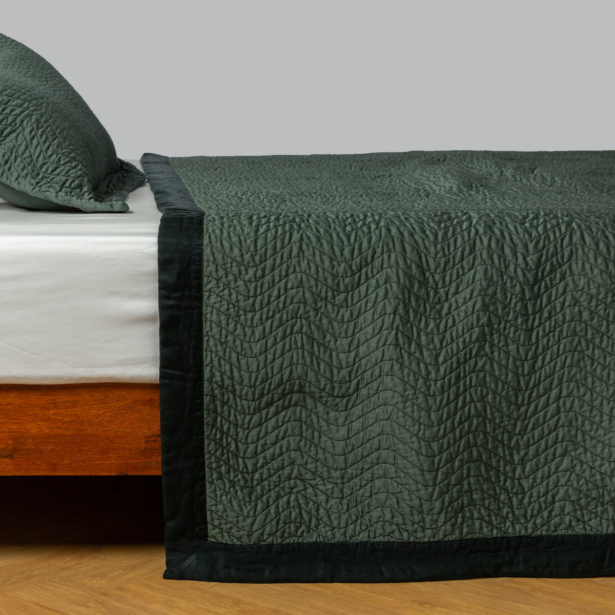 Cirillo coverlet in Juniper draped over bed foot, showing quilted texture and dark border trim.