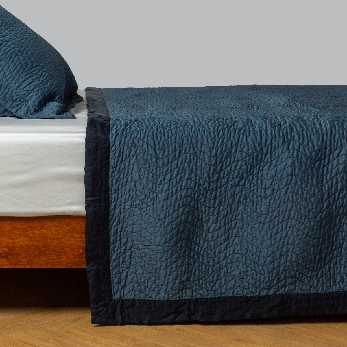Bella Notte Cirillo coverlet in Midnight draped over bed, showing quilted texture and contrast border trim.