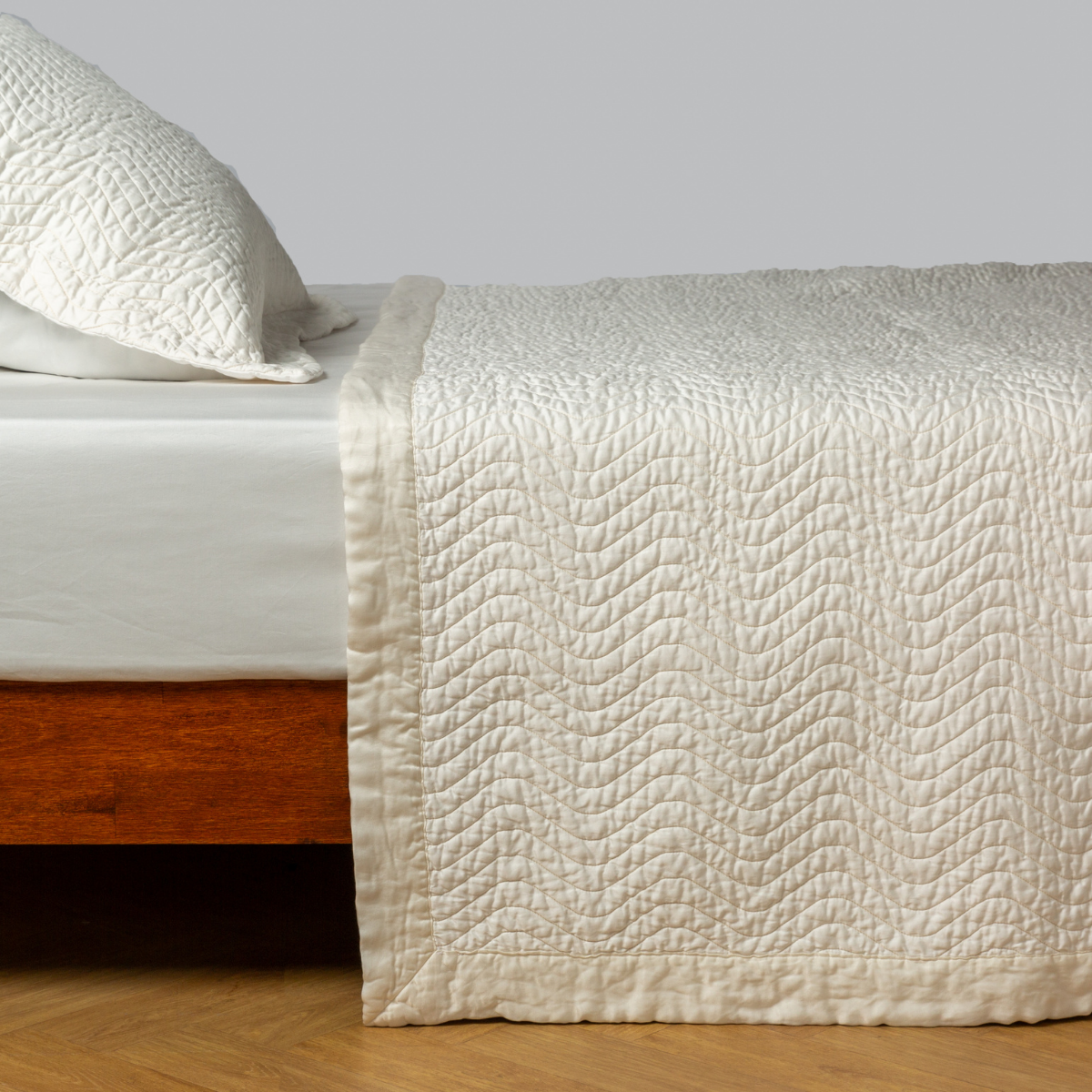 Bella Notte Cirillo coverlet in Winter White draped over bed, showing quilted wave stitching detail.