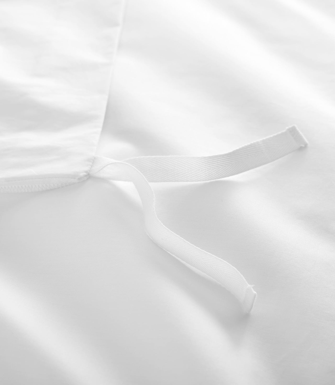 Close-up of white duvet cover interior corner tie on smooth cotton fabric.