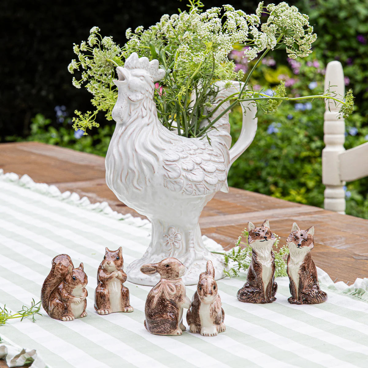 Brown ceramic bunny shakers styled outdoors alongside woodland animal figurines and a white rooster vase.
