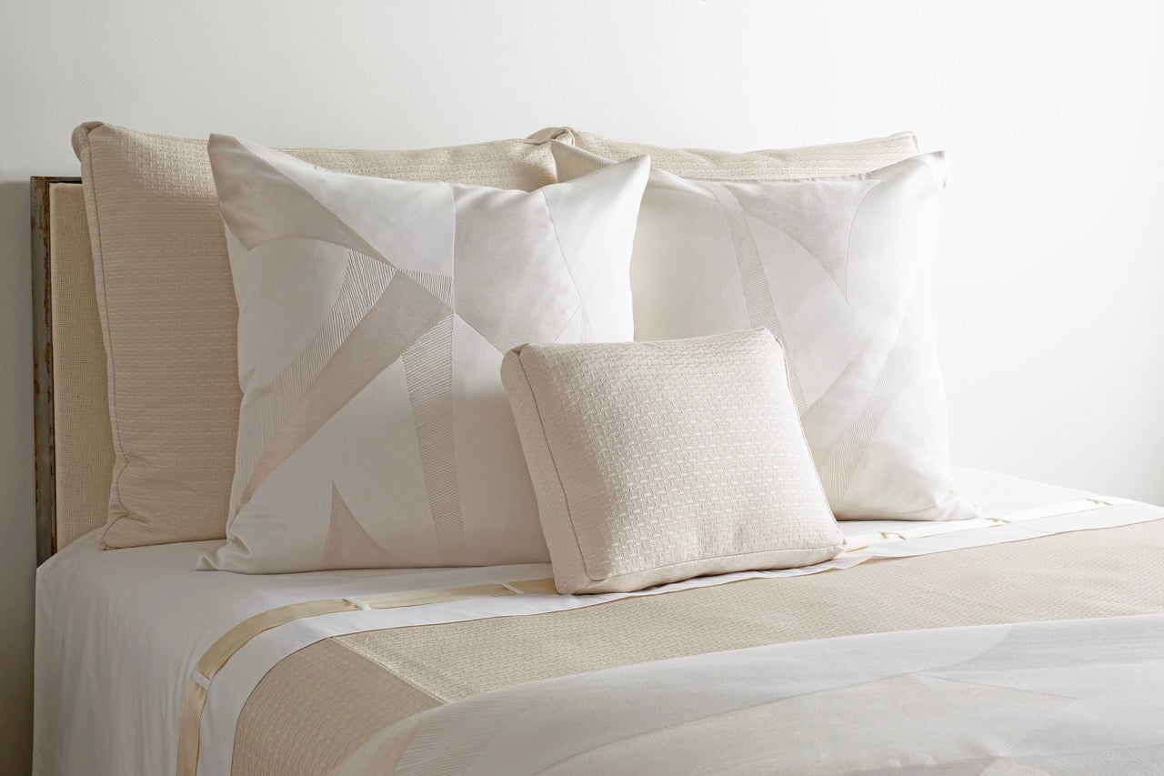 White and champagne bedding ensemble styled on a bed, featuring geometric pintuck pillows.