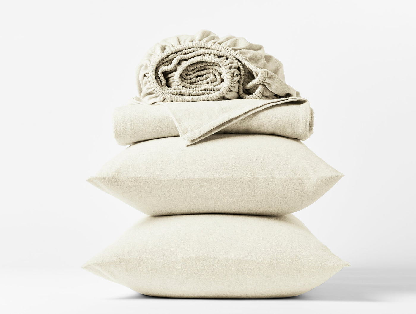 Stacked ivory flannel pillow shams and folded sheets with ruffled detail on white background.