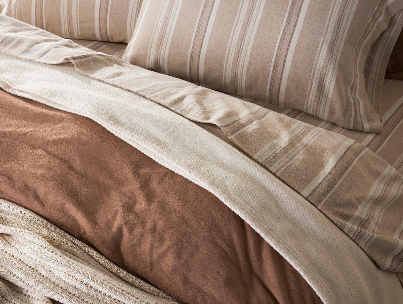 Ivory striped flannel sheets layered over terracotta bedding, angled close-up view.