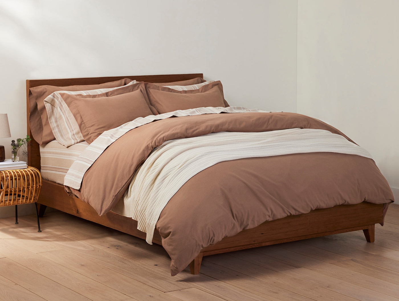 Ivory striped flannel sheets layered under a terracotta duvet on a mid-century wooden bed.