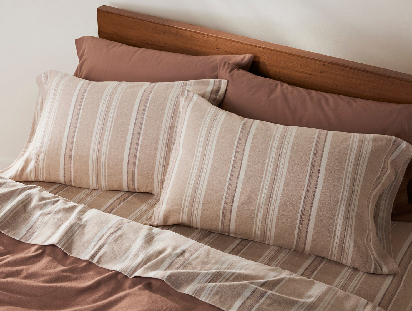 Coyuchi Cloud Brushed Flannel pillowcases in tan with white stripes styled on a made bed.